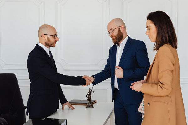 Two men shaking hands while a woman stands next to them